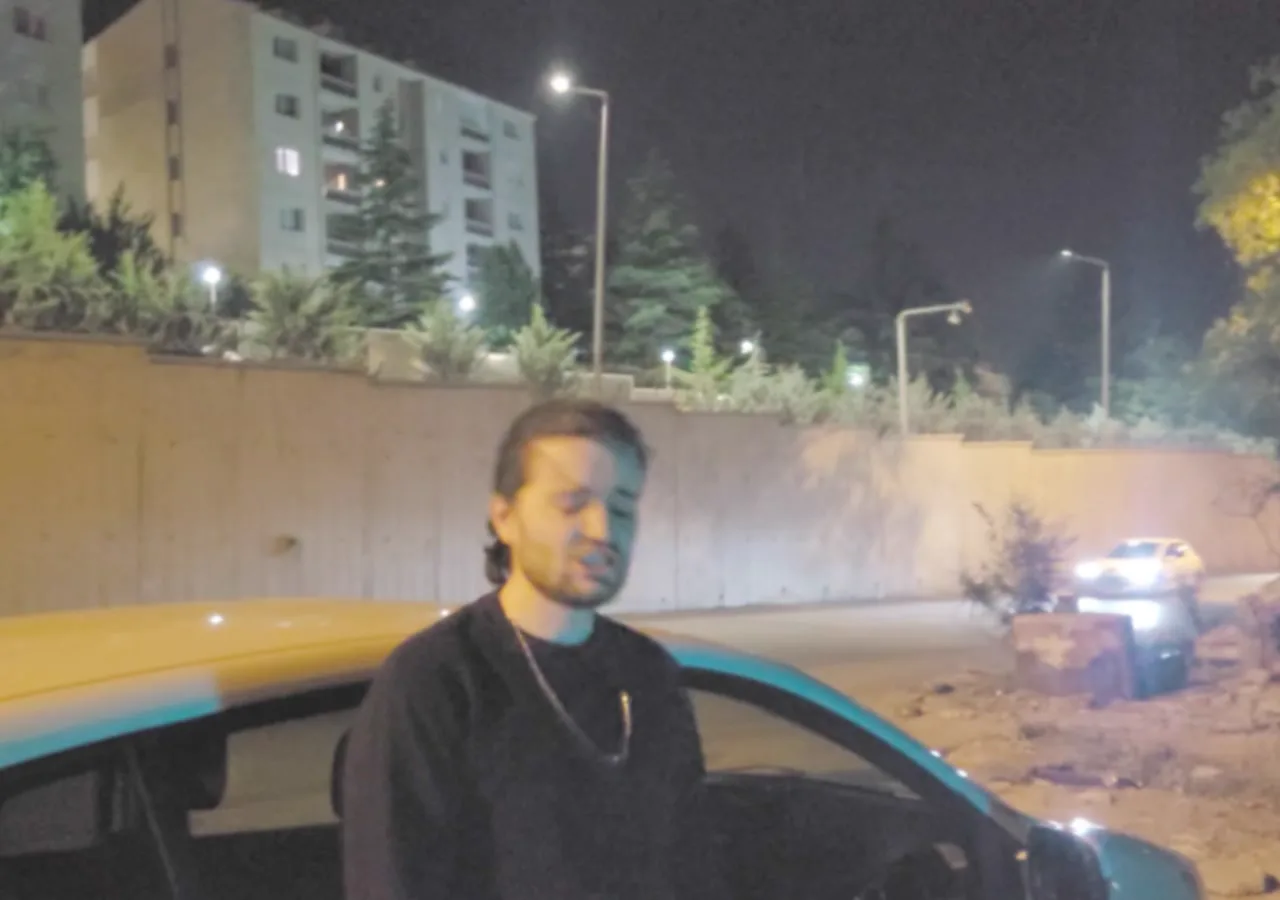 Binaların önünde, arabanın yanında duran Şahbender